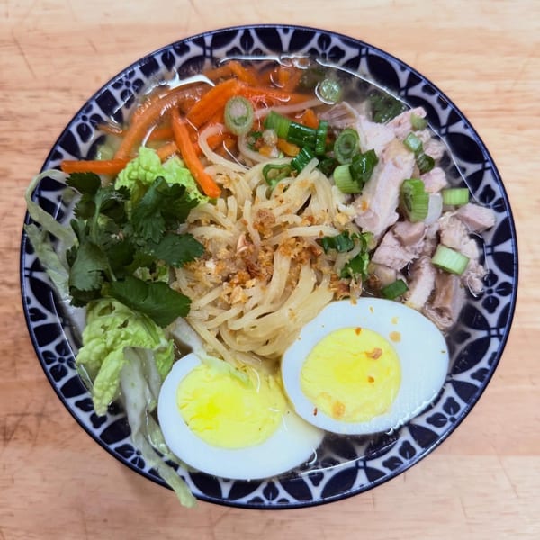 Overhead view of CheBogz Filipino chicken noodle soup with eggs, carrots, and greens.