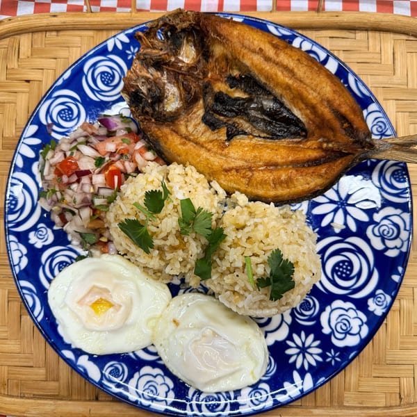 Filipino fried milkfish, garlic rice, two fried eggs, and tomato-onion relish on a blue and white plate.