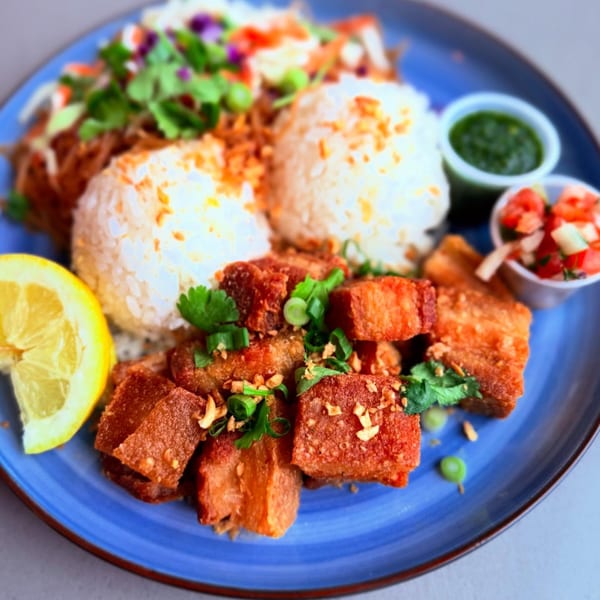Crispy pork belly (Lechon Kawali) with rice, salad, lemon, and dipping sauces on a blue plate.