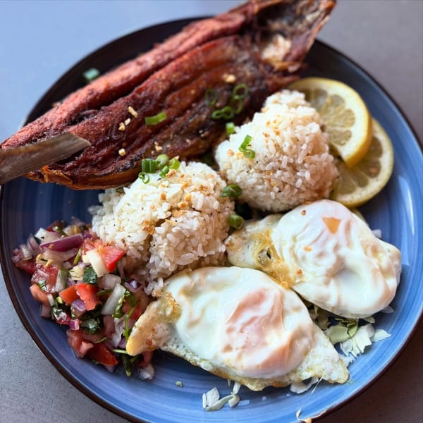 A Filipino dish with fried fish, garlic rice, two fried eggs, and tomato salsa on a blue plate.