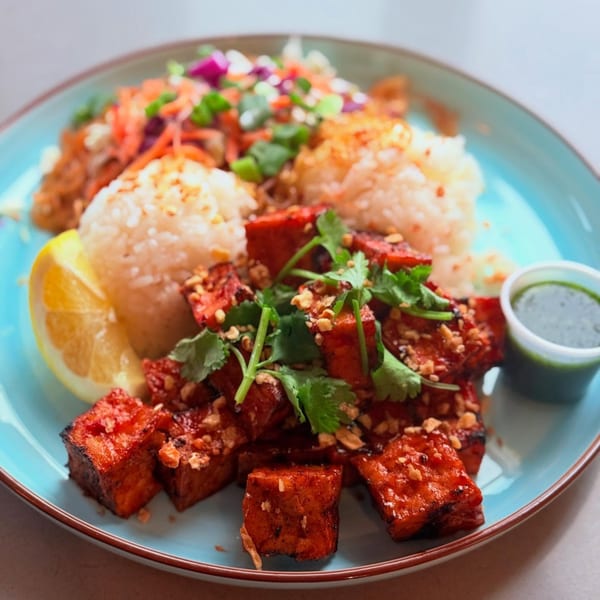 CheBogz Filipino dish with red tofu, white rice, shredded vegetables, lemon, and green sauce.