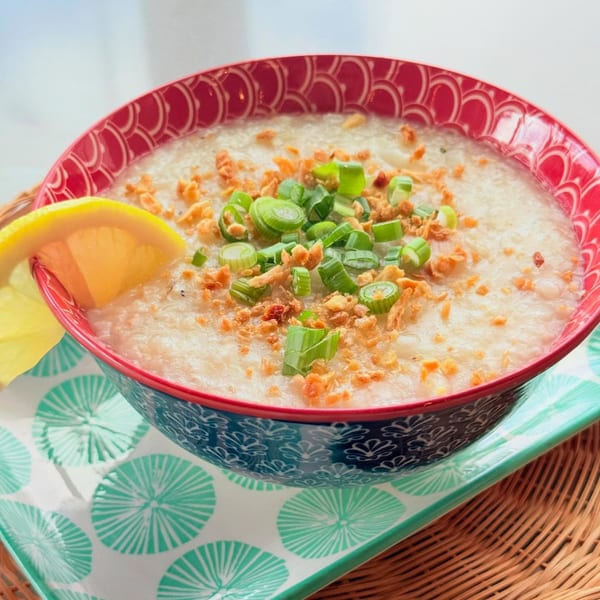 Filipino arroz caldo, a rice porridge, topped with green onions, fried garlic, and a lemon slice.